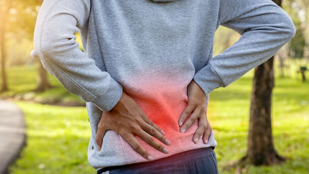 Muscle Imbalance and the Causes of Chronic Back Pain: What You Need to Know Photo of person in grey sweatshirt with both hands on lower back. A red glow on lower back to indicate where pain is. 