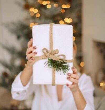 Person holding white gift box with pine tree branch