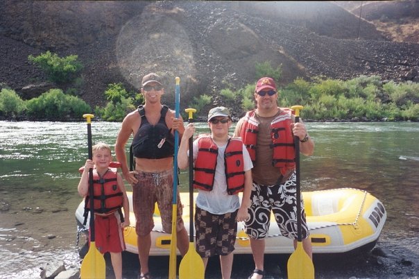 Family of four in front of yellow raft holding paddles